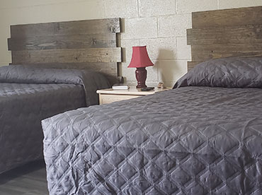 Inside motel room with two queen beds that are tastefully made and new, wooden headboards