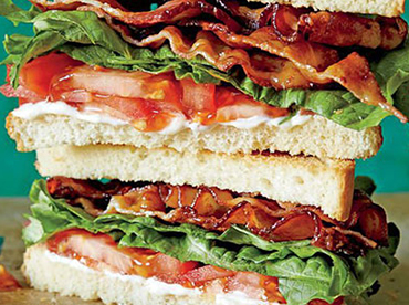 BLT sandwich double stacked with crisy bacon, lettuce, tomato and white bread shown on a wooden, cutting board 